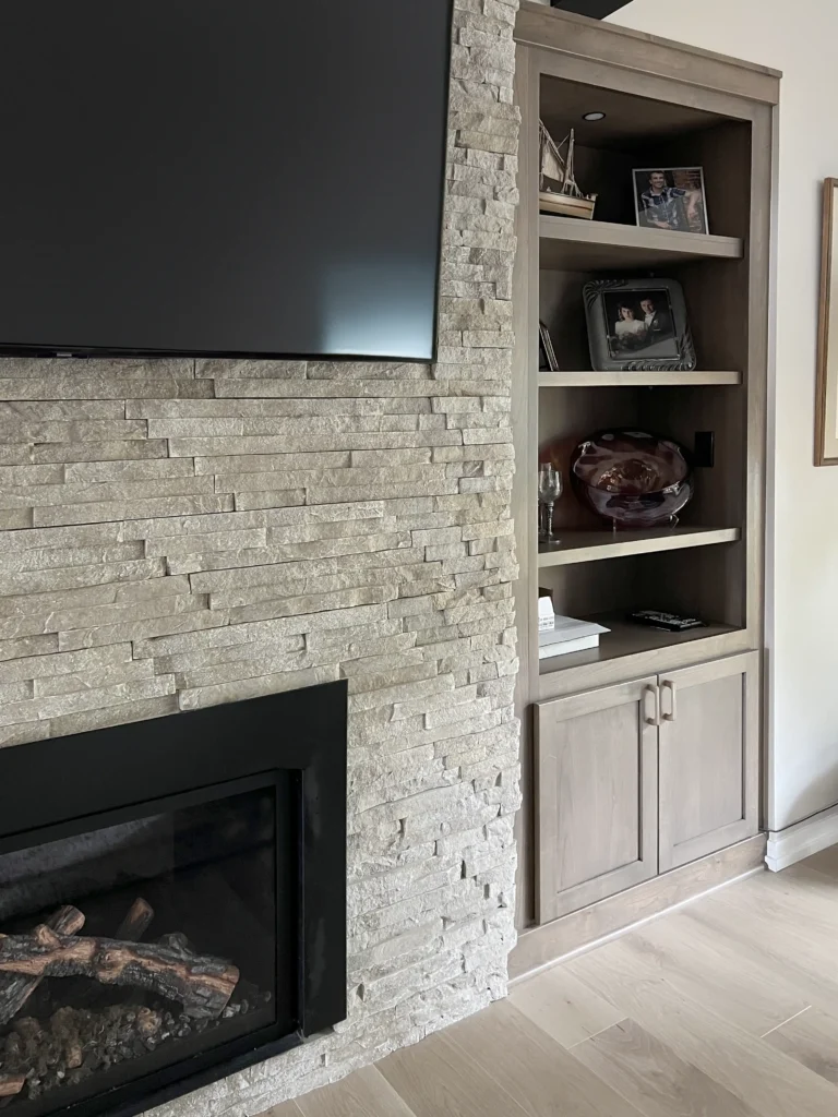 Stone fireplace wall with a television and adjoining built-in shelves and cabinets.