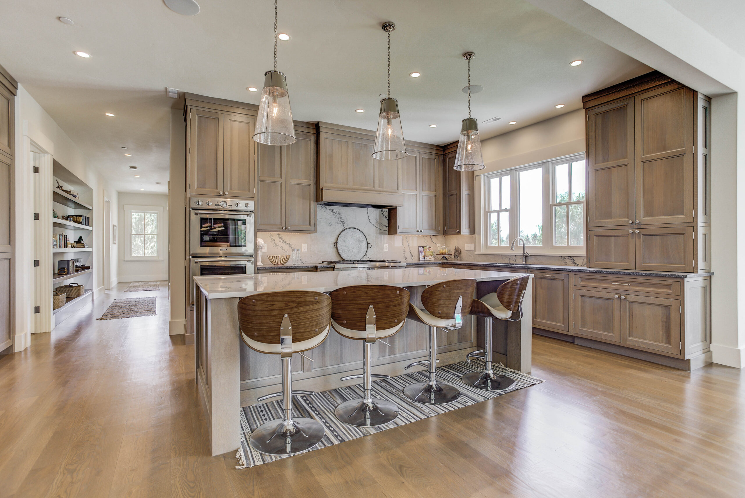 Spacious luxury kitchen with framed inset Crystal cabinetry, waterfall island, modern pendant lighting, and built-in appliances — contemporary kitchen design by Caitrin McLivain.