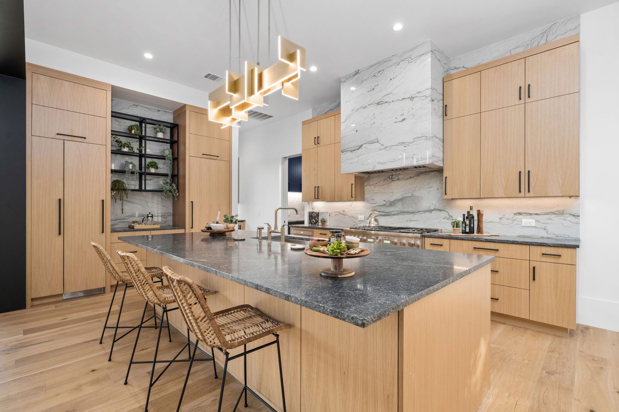 Modern luxury kitchen with natural rift cut white oak Crystal cabinetry, full-height quartz backsplash, large island with dark granite countertop, designer pendant lighting, and integrated refrigeration — CJ Bigini.