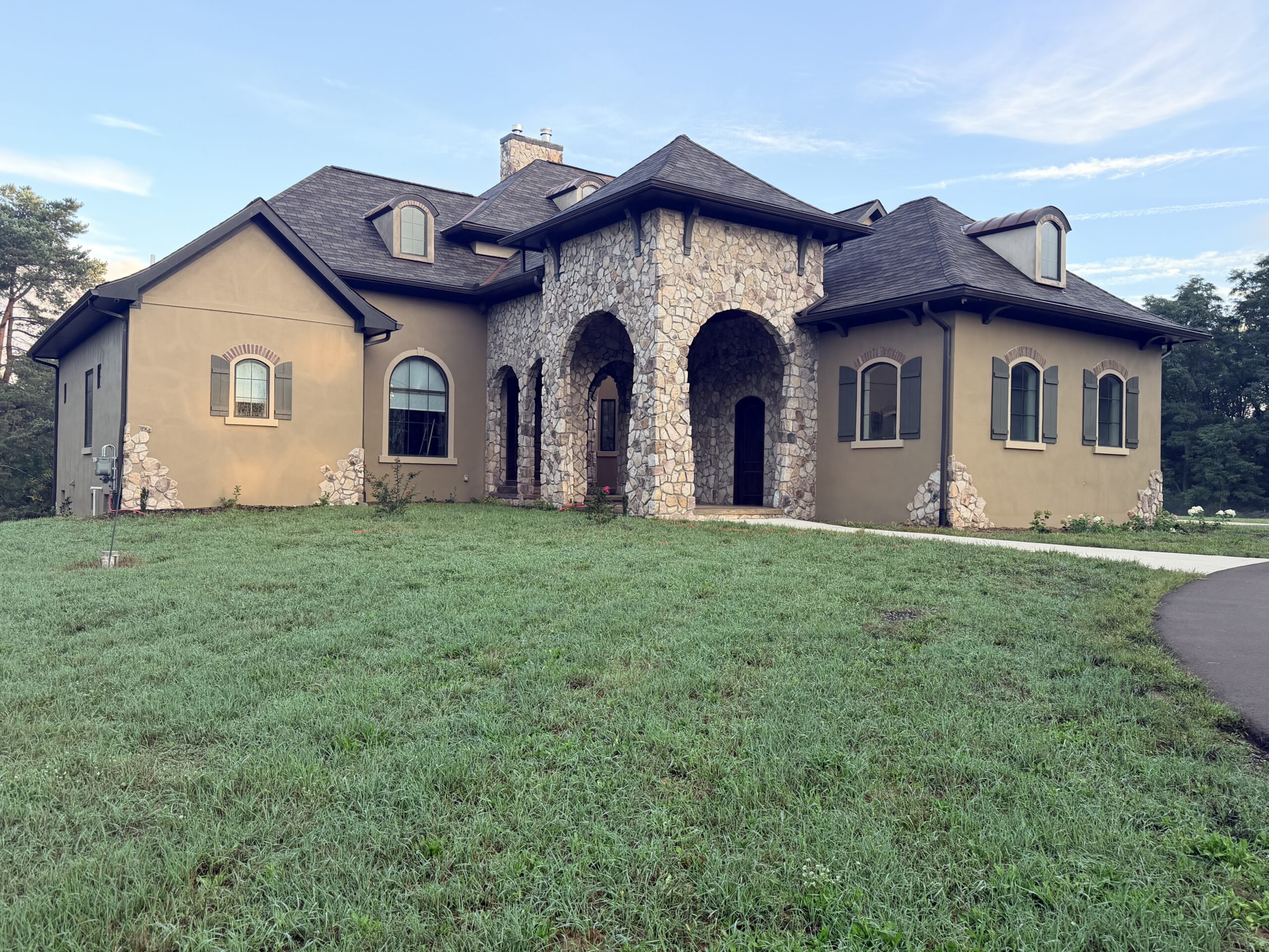 Stone and stucco home with an arched entry, tiled roof and broad lawn.